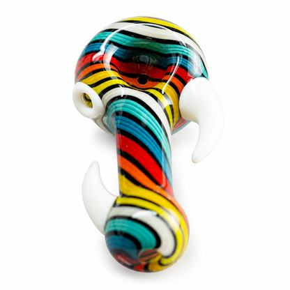 A colorful glass smoking pipe shaped like an elephant, featuring a striped pattern of red, yellow, teal, black, and white, with white tusks, photographed on a white background.